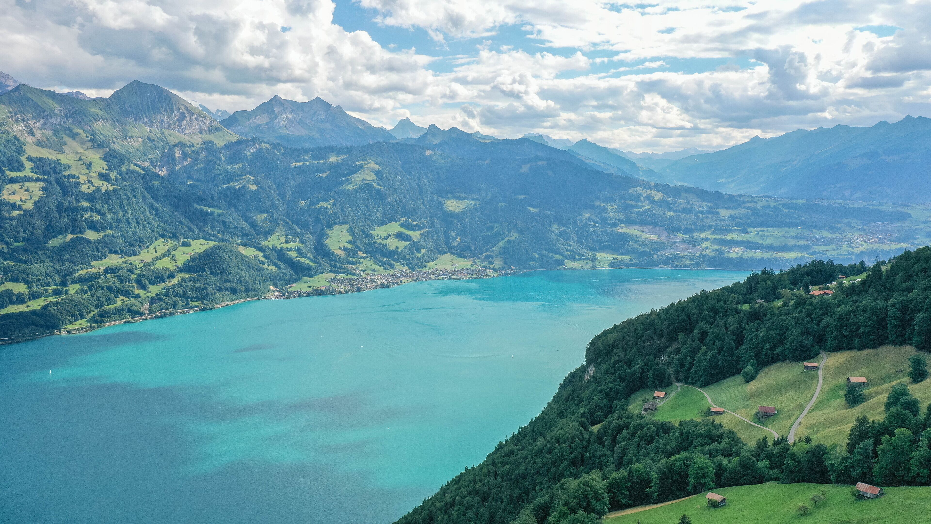 Una vista panorámica de un paisaje montañoso con un lago turquesa grande, rodeado de vegetación exuberante y montañas distantes.