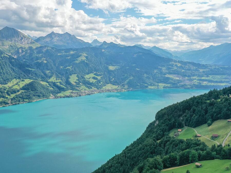 Una vista panorámica de un paisaje montañoso con un lago turquesa grande, rodeado de vegetación exuberante y montañas distantes.