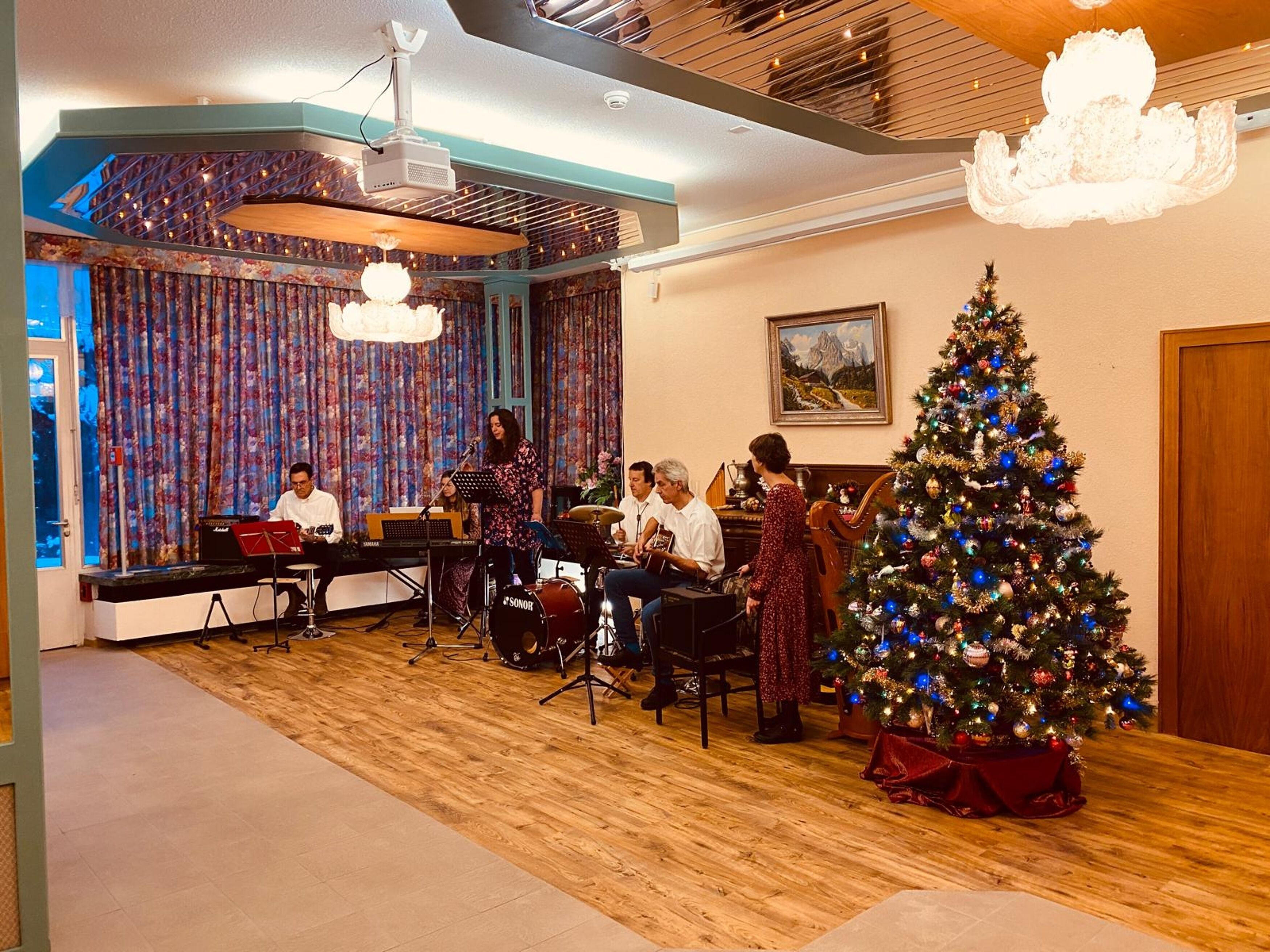 A room with a Christmas tree, a piano, and a group of people playing instruments.