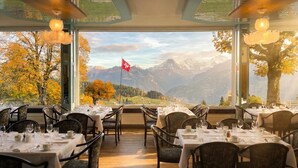 Ein Restaurant mit gedeckten Tischen, einer Schweizer Flagge und Blick auf die Berge.