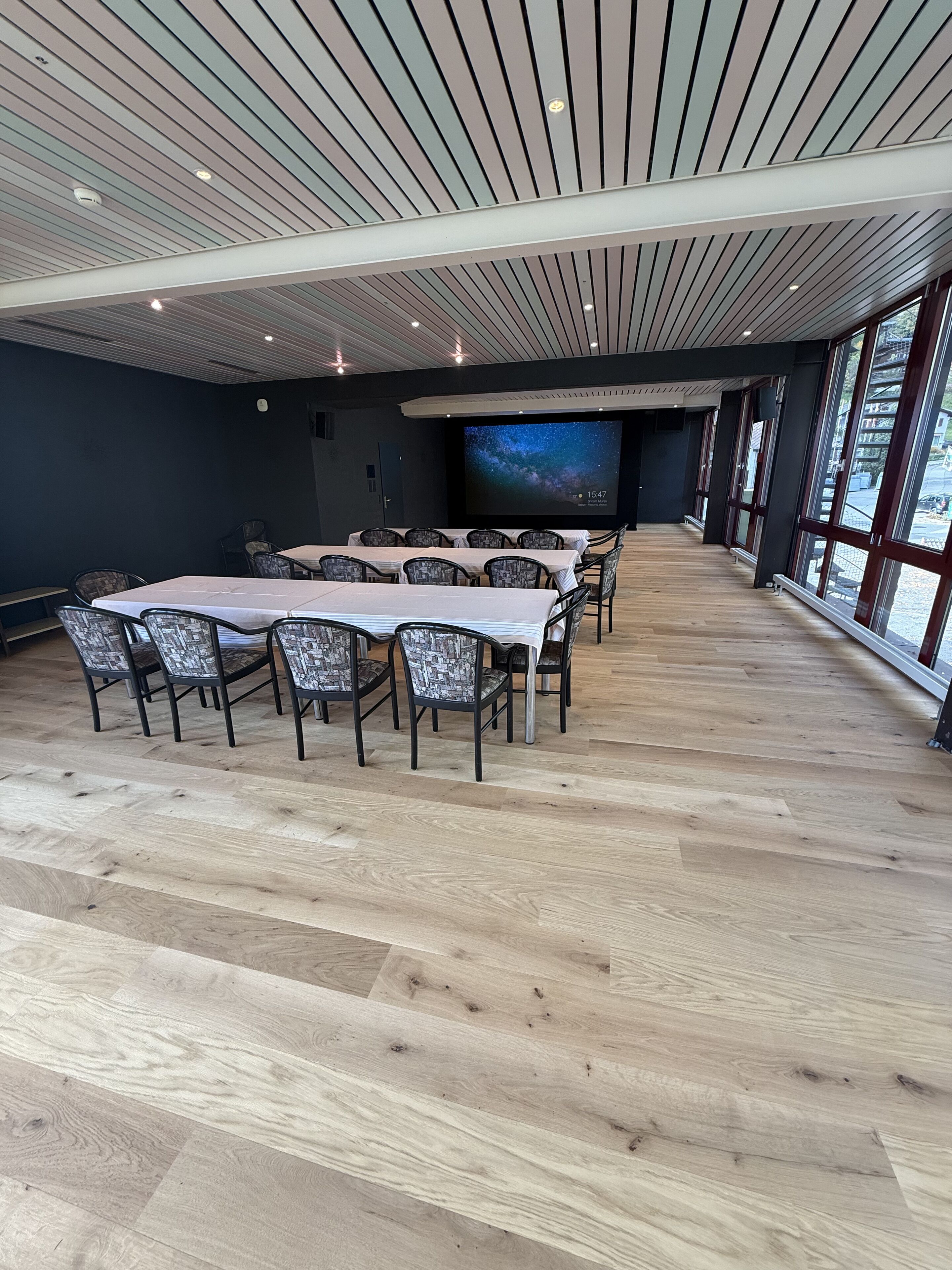 Un salón de conferencias con una pantalla grande que muestra un cielo estrellado, suelo de madera y sillas modernas.