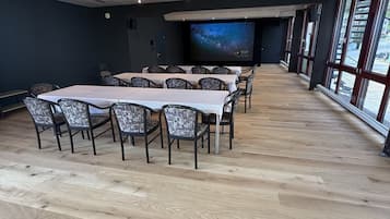 Un salón de conferencias con una pantalla grande que muestra un cielo estrellado, suelo de madera y sillas modernas.