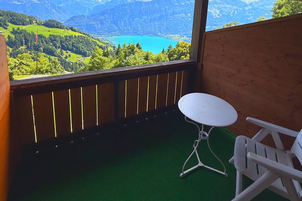 Un balcón con vistas a montañas y un lago, una mesa blanca y una silla blanca.