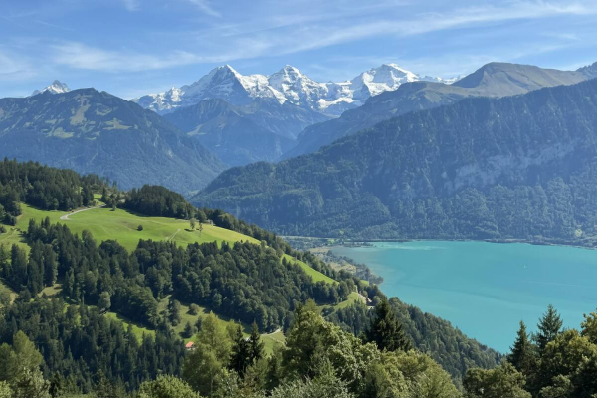 Un paisaje montañoso con un lago, zonas boscosas y picos nevados.
