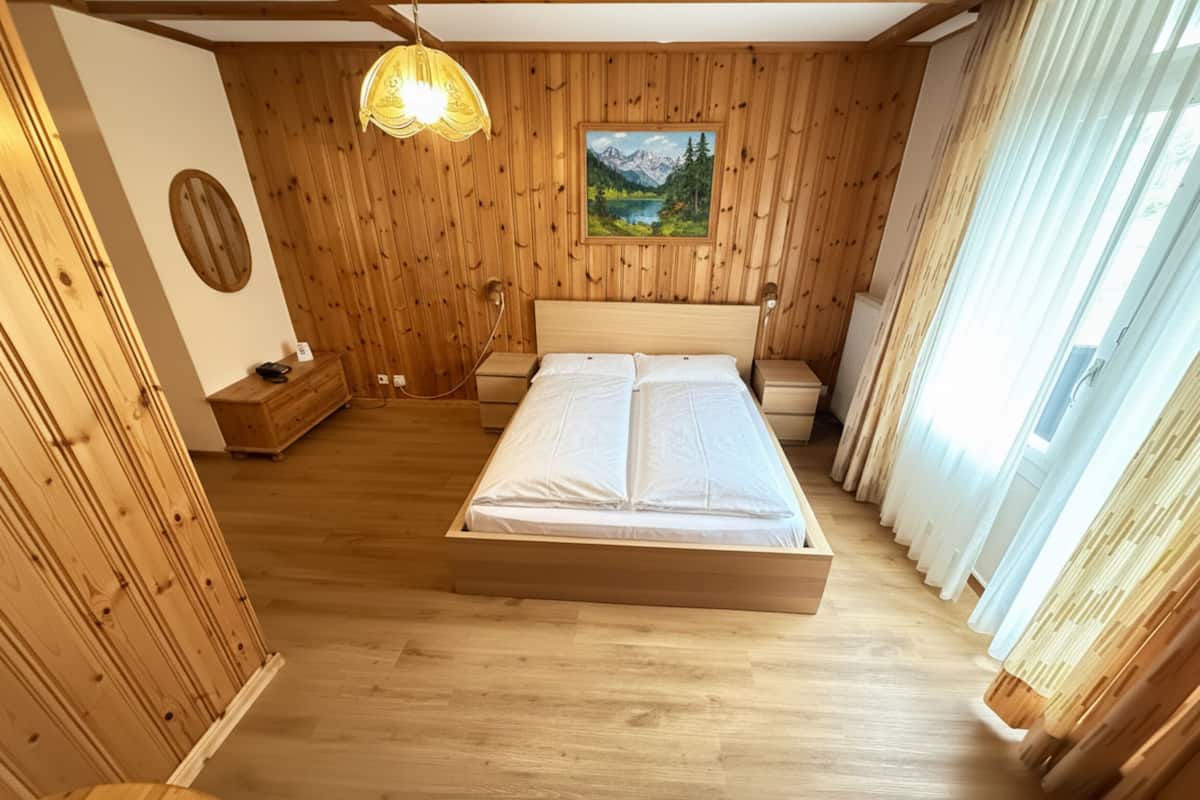 Una habitación con paneles de madera, una cama, un cuadro en la pared y una lámpara colgante.