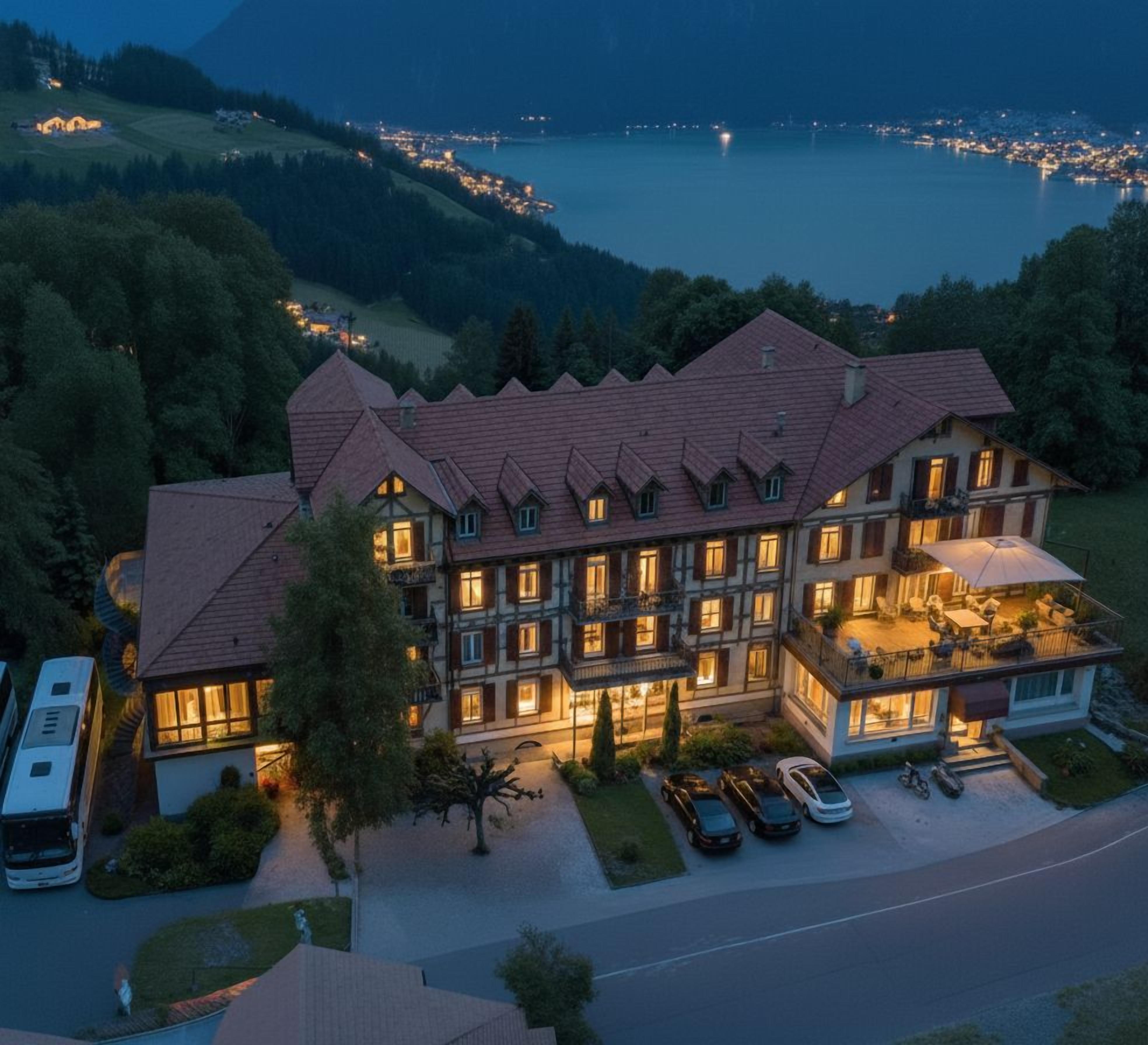 Un grande hotel a più piani con tetto in tegole rosse, numerosi balconi e vista sul lago al crepuscolo.