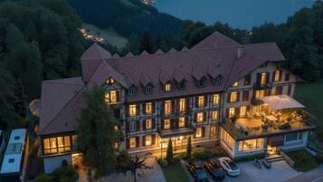 Un grande hotel a più piani con tetto in tegole rosse, numerosi balconi e vista sul lago al crepuscolo.
