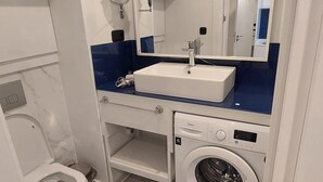 A modern bathroom with a white sink, mirror, and a washing machine. - Beautiful Studio Apartment in Batumi (Batumi)