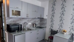 Ett kompakt kök med en inbyggd mikrovågsugn, en diskho och en liten matplats med en stol och ett bord.