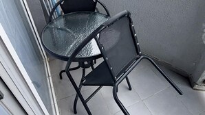 A balcony with a glass table and two chairs, a window, and a view of a multi-story building in the background. - Orbi Sea Towers Batumi (Batumi)
