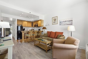 A spacious living area with a kitchen, wicker furniture, and a view of the sea.