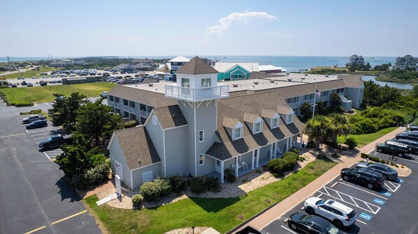 A large building with multiple floors, a parking lot, and a view of the ocean. - The Hatteras Ketch | 1 Bedroom Near-Beach Condos with Pool Access! (Hatteras)
