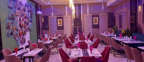 A restaurant with multiple tables and chairs, a colorful mural on the wall, and a modern ceiling design.