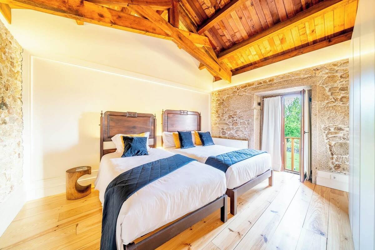 A bedroom with two beds, stone walls, wooden flooring, and a balcony with a view.
