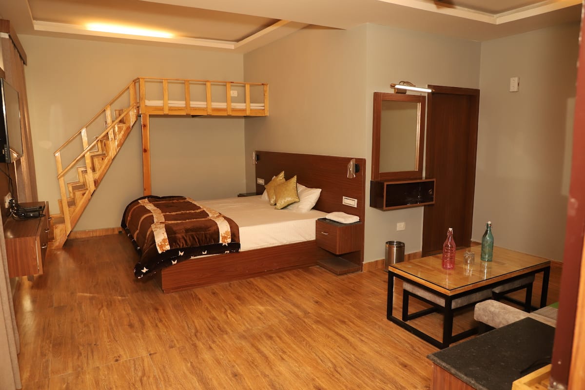 A bedroom with a wooden bunk bed, a small bedside table, a nightstand, a wooden desk, and a mirror.