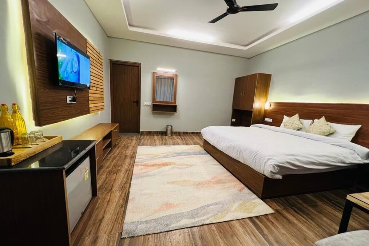 A modern hotel room with a bed, bedside table, TV, ceiling fan, and a small kitchenette.