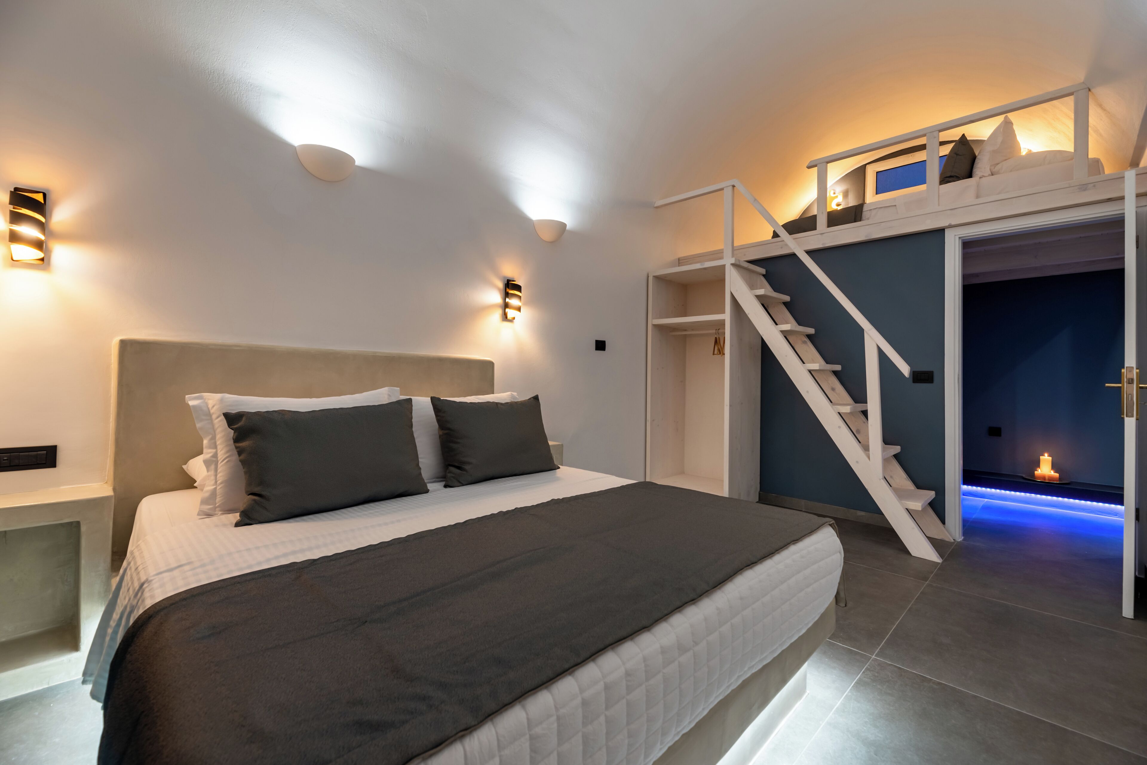 A modern bedroom with a bed, bedside tables, a built-in wardrobe, and a staircase leading to an upper level.