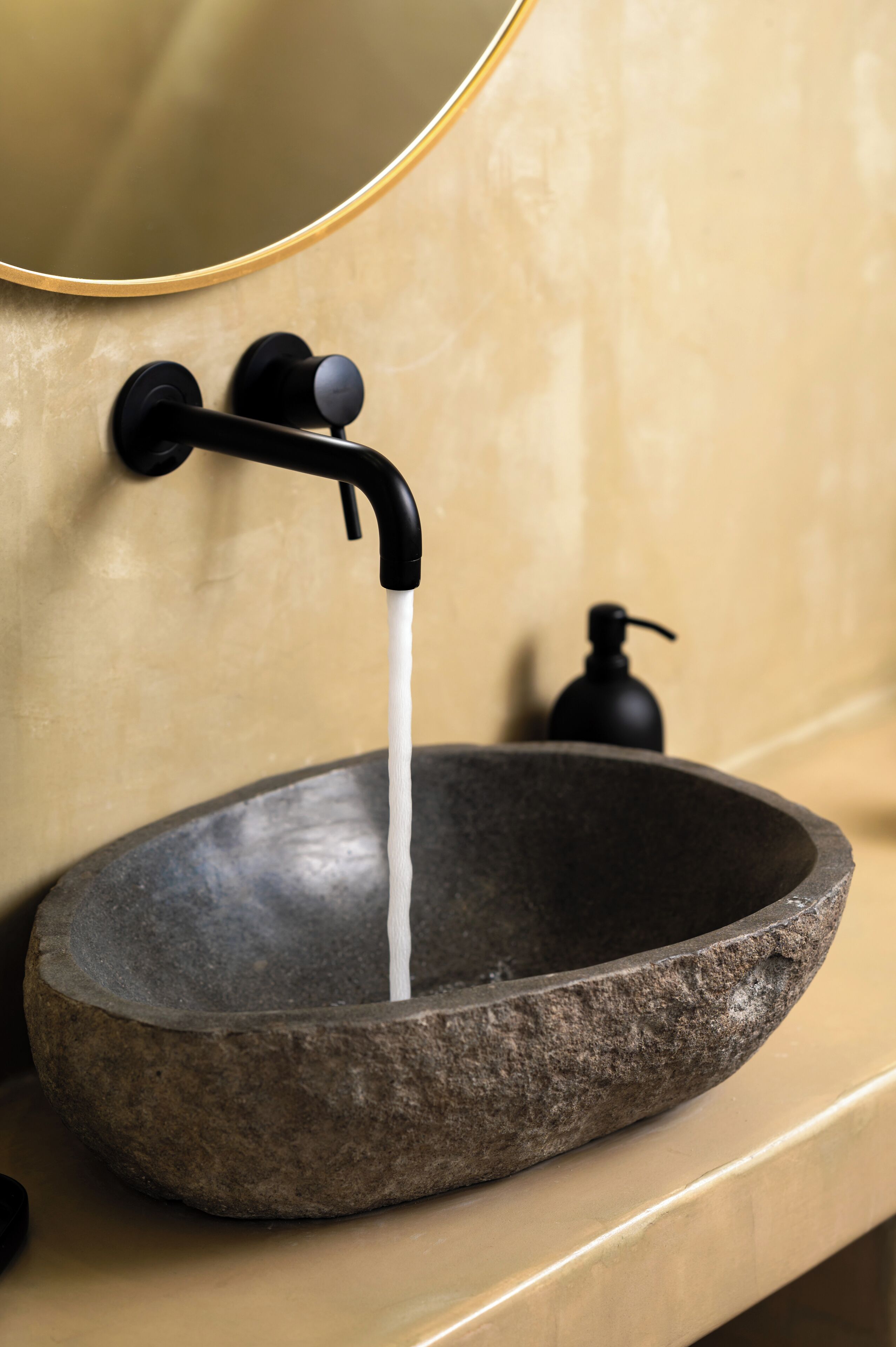 Ein Waschbecken aus Stein mit einem schwarzen Wasserhahn und einer Seifenspender.