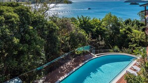 Una piscina con cubierta de madera, rodeada de exuberante vegetación y con vista a una extensa masa de agua y a islas distantes.