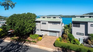 Un área residencial costera con dos casas modernas, un cielo azul despejado y vista al mar.