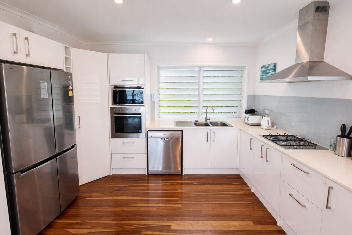 A modern kitchen with white cabinets, stainless steel appliances, a dishwasher, a microwave, a stove, and a window with blinds.