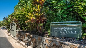 Schild mit der Aufschrift 'POINCIANA', eine Steinmauer und üppiges Grün im Hintergrund.