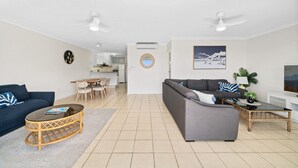 Ein modernes Wohnzimmer mit einem grauen Sofa, einem blauen Sitzsofa und einem Essbereich mit einem runden Tisch und Stühlen.