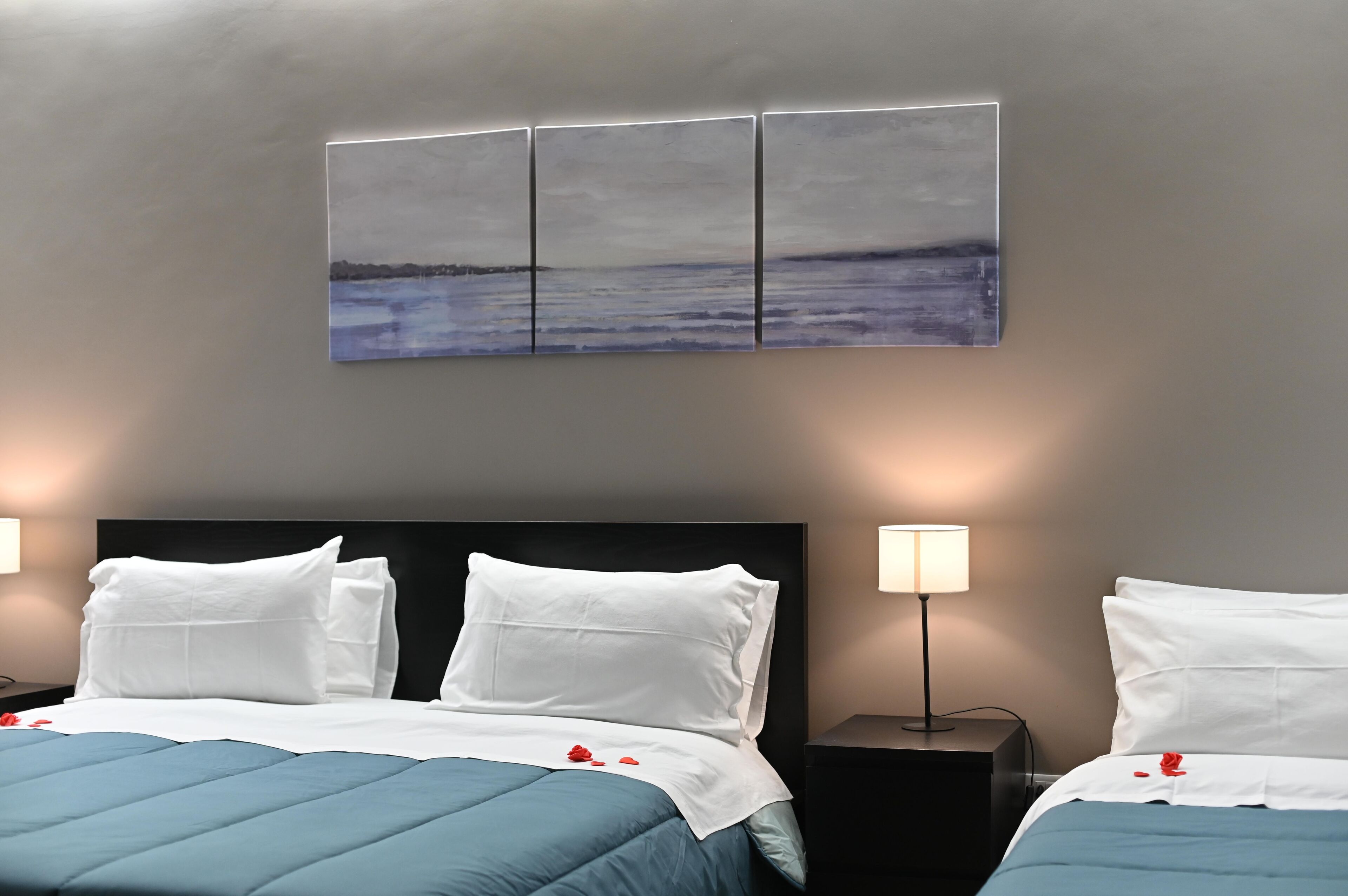 A hotel room with a bed, two bedside tables, a wall-mounted artwork, and a nightstand with a lamp.