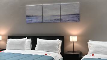 A hotel room with a bed, two bedside tables, a wall-mounted artwork, and a nightstand with a lamp.