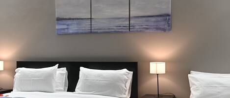 A hotel room with a bed, two bedside tables, a wall-mounted artwork, and a nightstand with a lamp.