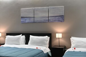 A hotel room with a bed, two bedside tables, a wall-mounted artwork, and a nightstand with a lamp.