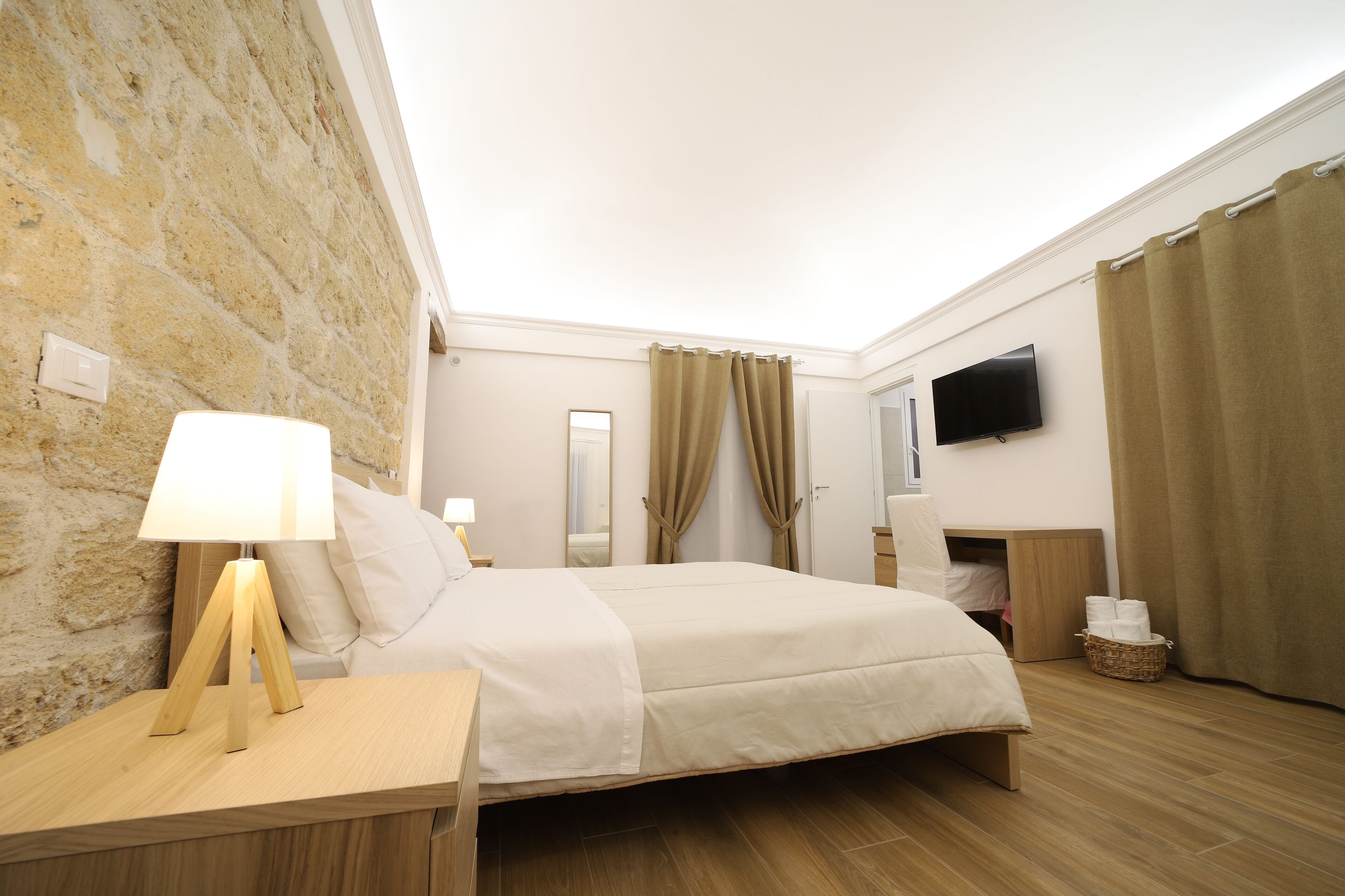 Een hotelkamer met een bed, nachtkastje met lamp, televisie aan de muur en een stenen muur.