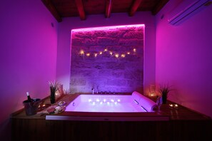 A spa room with a stone wall, a bathtub, candles, and a bottle of wine. - Boscò Suites (Carini)