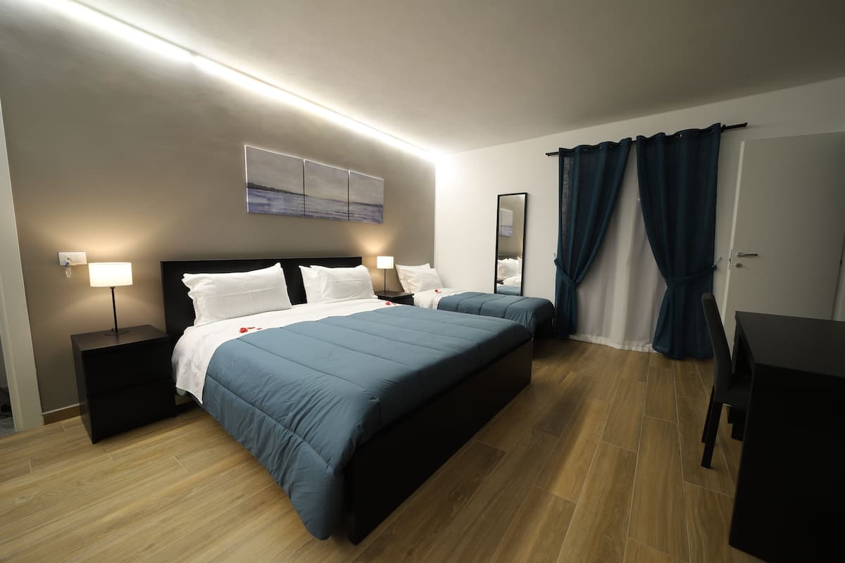 Une chambre d’hôtel moderne dotée d’un grand lit, de tables de chevet avec des lampes, d’un téléviseur à écran plat et d’une grande fenêtre avec des rideaux.