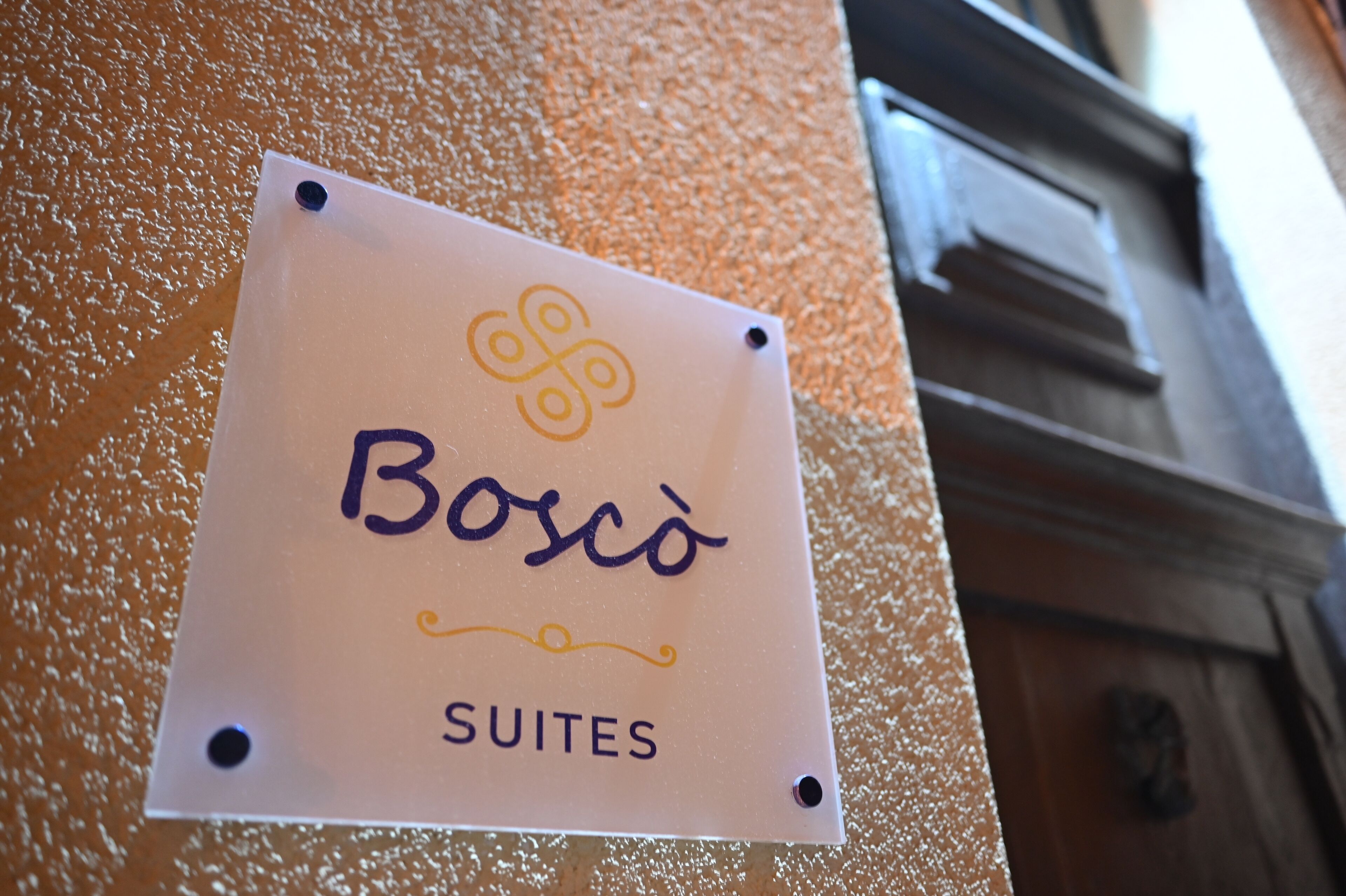 A sign for Bosco Suites on a textured wall.
