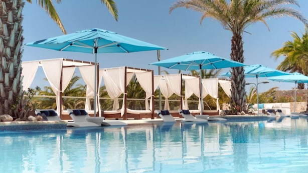 Zona de piscina con sillones, sombrillas y cabañas.