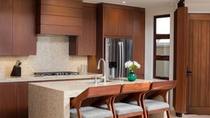 Una cocina moderna con armarios de madera, un refrigerador de acero inoxidable, encimera de granito y una zona de bar con taburetes.