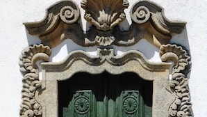 Una puerta verde con tallas intrincadas, ubicada en una pared blanca con adornos de piedra.