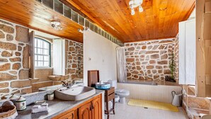 A bathroom with stone walls, wooden ceiling, a sink, toilet, and bathtub.