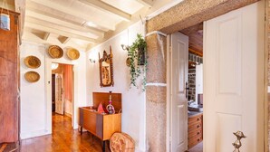 A hallway with wooden flooring, a wooden bench, a stone pillar, and a door leading to a room with a sink and cabinets.