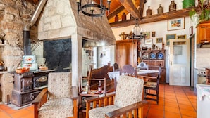 Un interior rústico con chimenea de piedra, mobiliario de madera y suelo de baldosas.