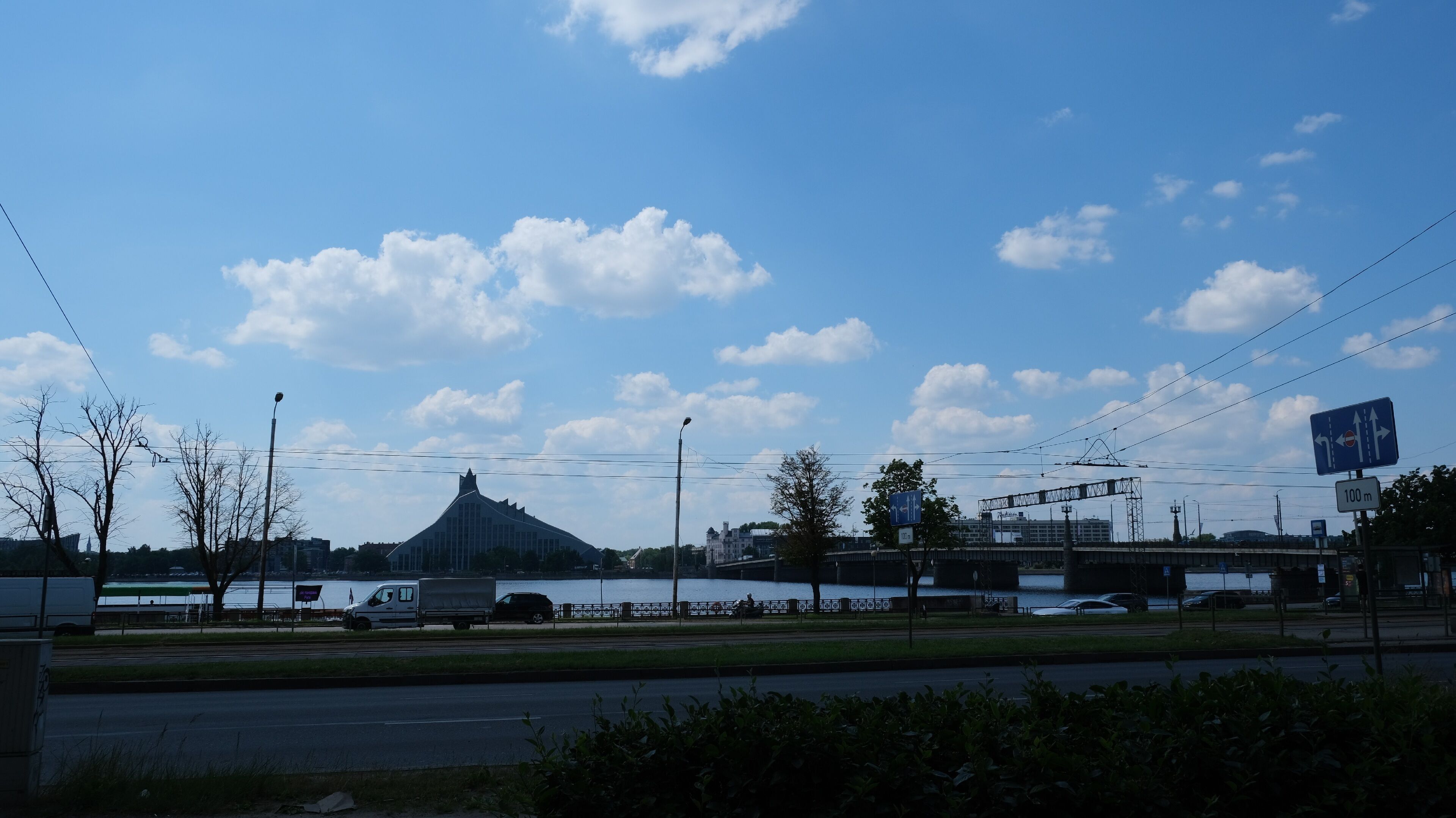 A view of a bridge with a large building in the background, a river, and a road with vehicles.
