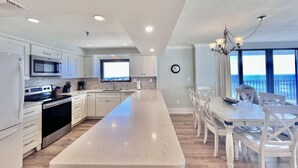 A modern kitchen with a long island, white cabinetry, stainless steel appliances, and a view of the ocean. - 2BR/2BA End Unit, Pool , Prvt Covered Parking, Seasonal Beach Serv. (Panama City Beach)