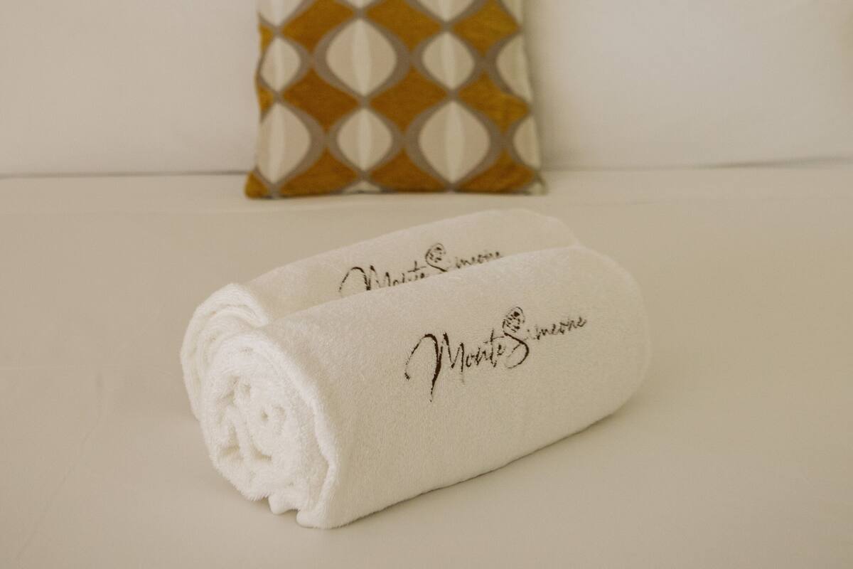 A neatly made bed with a rolled white towel and a pillow with a geometric pattern.