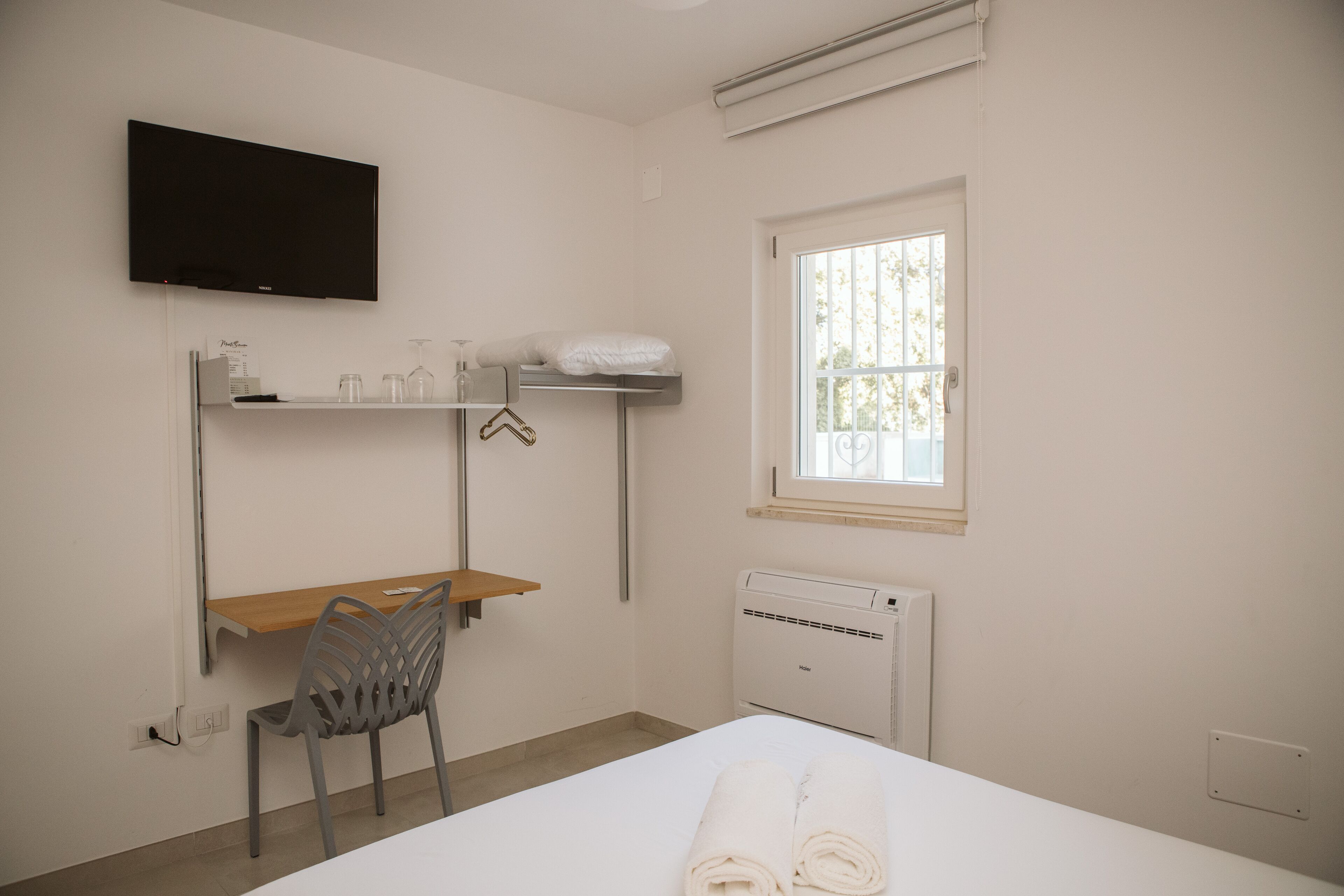 Ein Schlafzimmer mit Bett, Schreibtisch, Sessel, Fernseher, Fenster und Heizkörper.