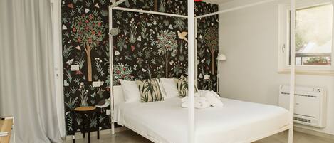 Un dormitorio con cama con dosel, papel tapiz floral negro, ventilador de techo blanco y ventana con vistas.