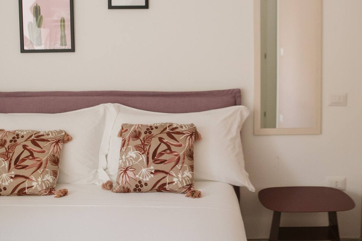 A bedroom with a bed, pillows, a bedside table, and framed pictures on the wall.