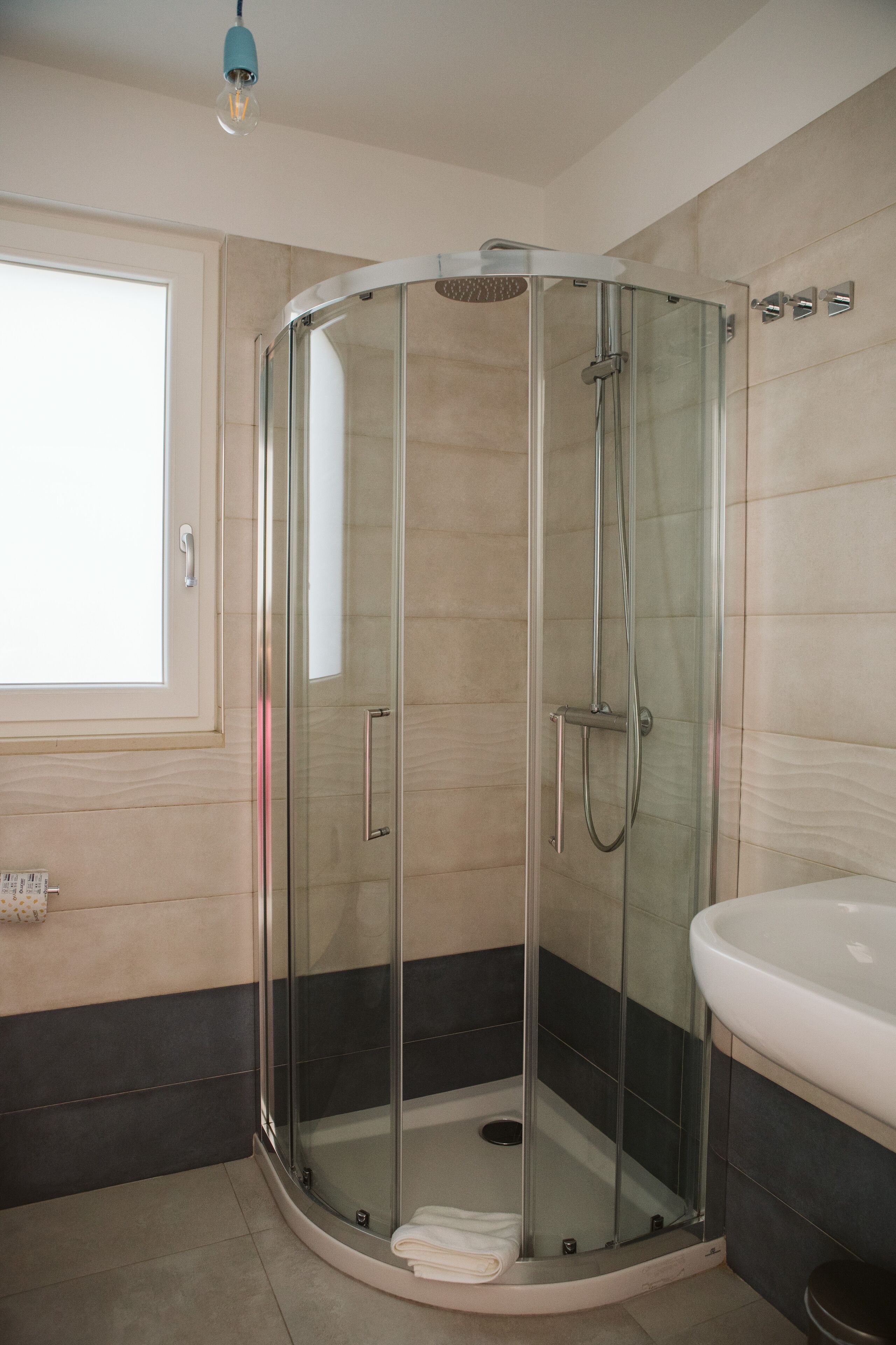 A modern bathroom with a glass-enclosed shower, a white sink, and a window providing natural light.