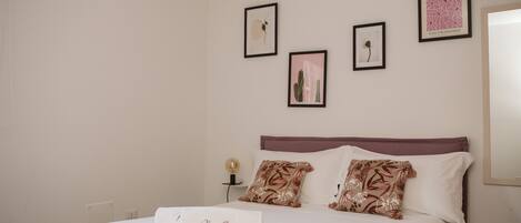 A neatly made bed with a white comforter and decorative pillows, a bedside table with a lamp, and framed artwork on the wall.