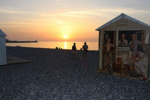 A pebbled beach with a small building labeled "Les bulots" and a sunset in the background.